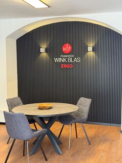 3D-Wandlogo von Francisco Wink Blas und ERGO auf schwarzer Lamellenwand im Besprechungsraum. rechts alttext: 3D-Wandlogo von NF Immobilien an einer hellen Wand im modernen Empfangsbereich.