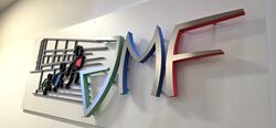 3D-Wandlogo des JMF Gymnasiums mit farbigen Grundkörpern und Edelstahlveredelung