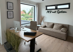 3D-Wandlogo „PKV mit System“ an einer hellen Bürowand über einem Sitzbereich.