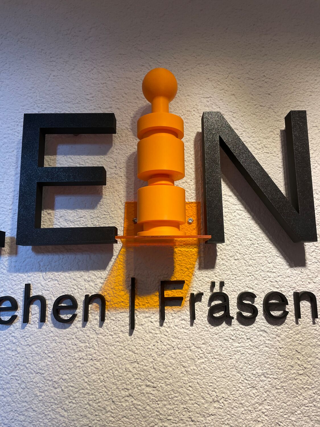 Wechselbares orangefarbenes 3D-Logo-Element mit individuell entwickelter Halterung bei Dauerlein